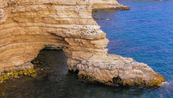 Steep rocky shore with an arch above the water with steppe vegetation, in eastern Crimea photo