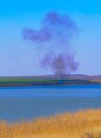 Fire at the lake shore, smoke from burning reeds in the background, Ukraine photo