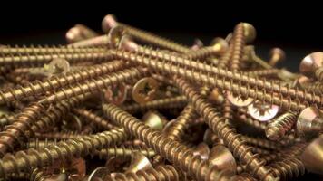 Close up view of a pile of gold screws. The screws are arranged in a random pattern and are illuminated by a bright light. The captures details of the screws, including the threads and the heads video