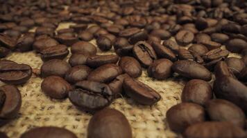 A close-up shot of roasted coffee beans scattered on a burlap surface. The beans are dark brown and shiny, with a deep, rich color. Coffee industry concept. Moving camera. video