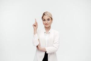 A middle-aged business woman in a white suit against studio background shows the emotions of a new idea. Gesture index finger up and pointing away. Business solutions concept. Banner advertising photo