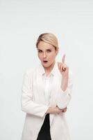 A middle-aged business woman in a white suit against studio background shows the emotions of a new idea. Gesture index finger up and pointing away. Business solutions concept. Banner advertising photo