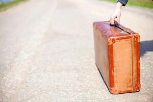 Old travel brown suitcase. Traveler stands on road. Single trip. photo