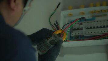 An electrician is using an electrical testing tool with his left hand turning the device to check the current in an electrical control box in a house. video