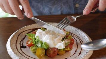 usinng fork and knife to eat italian greek salad food topped with fresh mozzarella cheese on the top home cooking style for appetizer in dinner time video