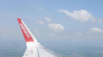 view through airplane aircraft window with wing view flying making a turn in sky above countryside farm field cloudyscape in sunny day video