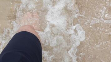view top down to barefooted feet while walking on sandy white ocean beach in luxury resort outdoors with sea wave splashing hitting feet. video