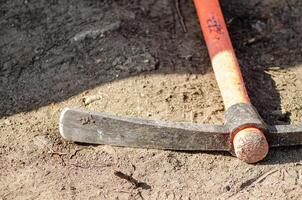 close-up of a pickaxe lying on the ground at a work site, featuring a red Kevlar handle. photo
