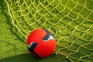 red soccer ball on the net of a goal in a football field photo