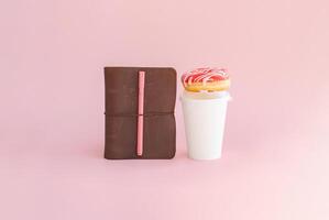 Donut on coffee cup and notebook with pen. Morning routine or study break concept. photo