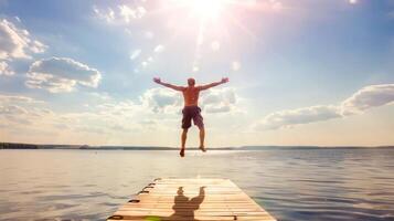 Man jumping off a wooden pier into a serene lake under a bright summer sun with a clear blue sky and fluffy white clouds photo
