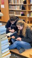 Students Studying Together in Library Surrounded by Bookshelves and Stacks of Books photo