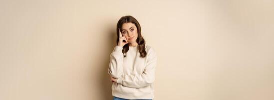 Annoyed woman, roll eyes and looking unamused, bothered and bored, standing over beige background photo