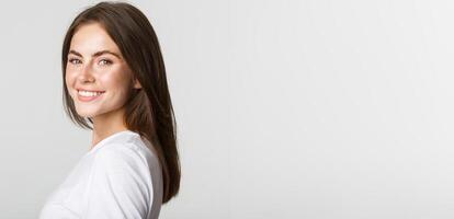 Portrait of confident beautiful brunette woman turning face at camera with dreamy look, smiling over white background photo