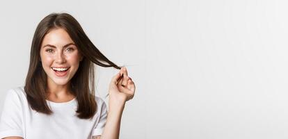 Portrait of flirty beautiful girl playing with hair and smiling at camera intrigued photo