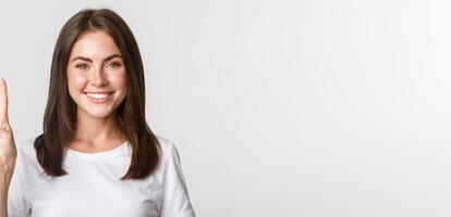 Portrait of beautiful and happy brunette girl smiling and showing peace gesture, standing white background photo