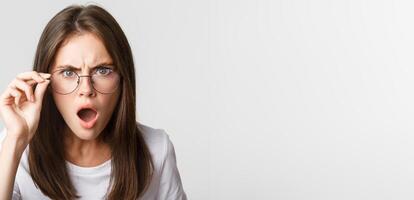Close-up of insulted and shocked young angry woman looking from under glasses photo