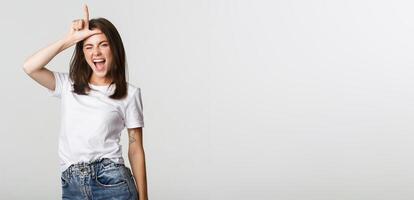 Sassy good-looking girl smiling and mocking person, showing loser gesture on forehead photo