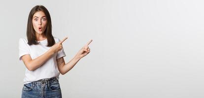 Impressed and amused brunette girl say wow and pointing upper right corner at banner photo