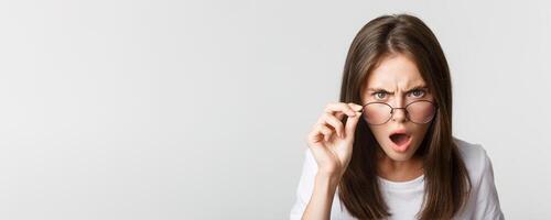 Close-up of insulted and shocked young angry woman looking from under glasses photo