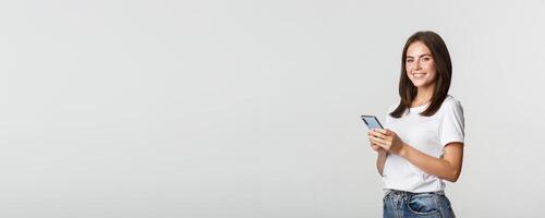 Attractive young brunette woman using mobile phone and smiling at camera photo