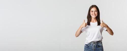Happy satisfied young woman smiling, showing thumbs-up in approval, like something photo