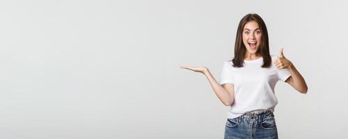 Satisfied attractive girl holding something on hand and showing thumbs-up in approval photo