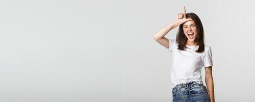 Sassy good-looking girl smiling and mocking person, showing loser gesture on forehead photo