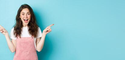 Pick your side. Smiling excited woman screaming of joy, pointing fingers sideways at left and right copy space, showing advertisement good deal, standing against blue background photo