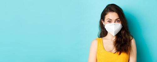 Covid-19, coronavirus and social distancing. Attractive young woman wearing respirator from coronavirus, looking at camera, blue background photo