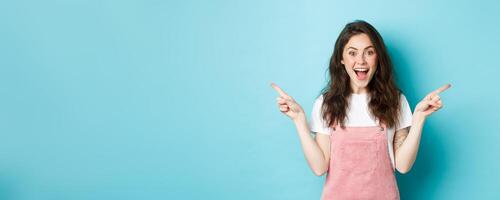 Pick your side. Smiling excited woman screaming of joy, pointing fingers sideways at left and right copy space, showing advertisement good deal, standing against blue background photo