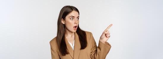 Portrait of businesswoman pointing finger left, showing corporate banner, logo, standing in brown suit over white background photo