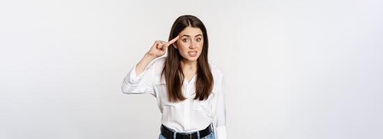 Are you dumb. Annoyed woman scolding, roll finger over head and staring at camera, bothered by someone crazy, standing over white background photo