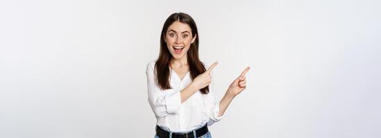 Portrait of enthusiastic smiling woman, female entrepreneur pointing fingers left and showing advertisement, showing announcement, white background photo