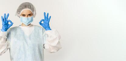 Image of healthcare worker, doctor in personal protective equipment from covid-19, showing okay ok sign, confident face in mask, standing over white background photo