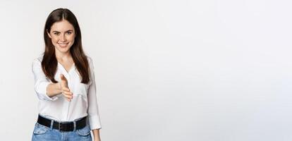 Smiling, friendly corporate woman extending arm for handshake, shaking hand, greeting business partner, standing over white background photo