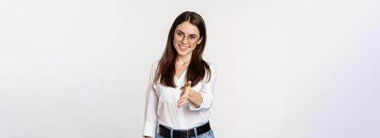 Corporate woman in office extending hand and smiling, handshake, greeting business partner, standing in glasses over white background photo