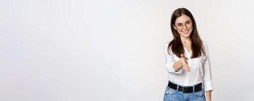 Corporate woman in office extending hand and smiling, handshake, greeting business partner, standing in glasses over white background photo