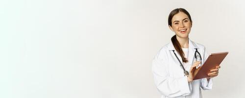 Doctor in white coat using digital tablet, reading medical data on gadget, working in hospital, standing over white background photo