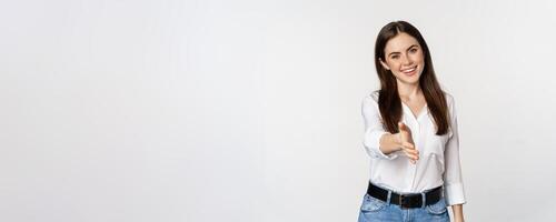Smiling, friendly corporate woman extending arm for handshake, shaking hand, greeting business partner, standing over white background photo