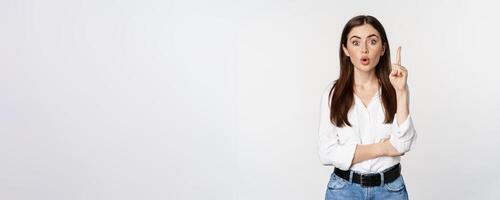 Portrait of woman raising finger, pointing up, suggesting smth, has solution, reveal smth, standing over white studio background photo