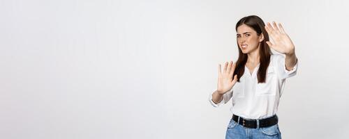 Displeased woman showing stop, rejection gesture, waving hands to decline, refuse of something ugly, standing over white background photo