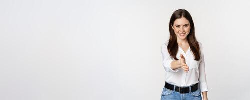 Smiling, friendly corporate woman extending arm for handshake, shaking hand, greeting business partner, standing over white background photo