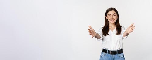 Enthusiastic laughing woman, smiling and stretching out arms forward, welcome you, greeting, standing over white background photo