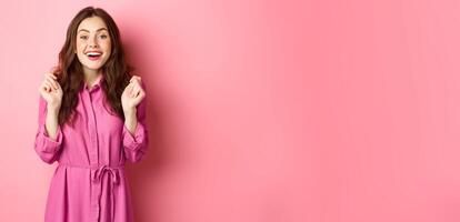 Excited brunette girl jumping hopeful, waiting for results, wants to get prize or win, standing against pink background photo