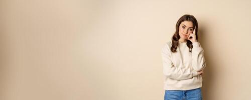 Annoyed woman, roll eyes and looking unamused, bothered and bored, standing over beige background photo