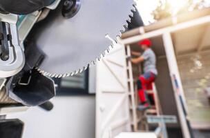 Construction Worker Using a Circular Saw While Standing on a Ladder at a Residential Site photo