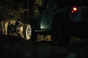 Man Inspecting Tire of AWD Vehicle in Dense Forest During Evening photo