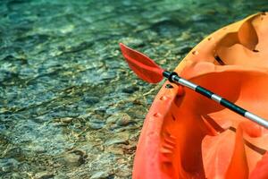 Bright Orange Kayak With Paddle Resting on Clear Water Surface photo
