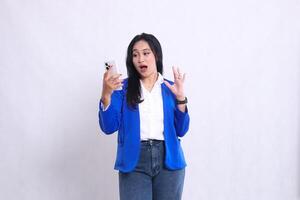 beautiful young office woman wearing blue formal suit standing shocked candid operating smartphone handphone while her hand sideways away from cellphone. for technology , lifestyle, mobile transaction photo